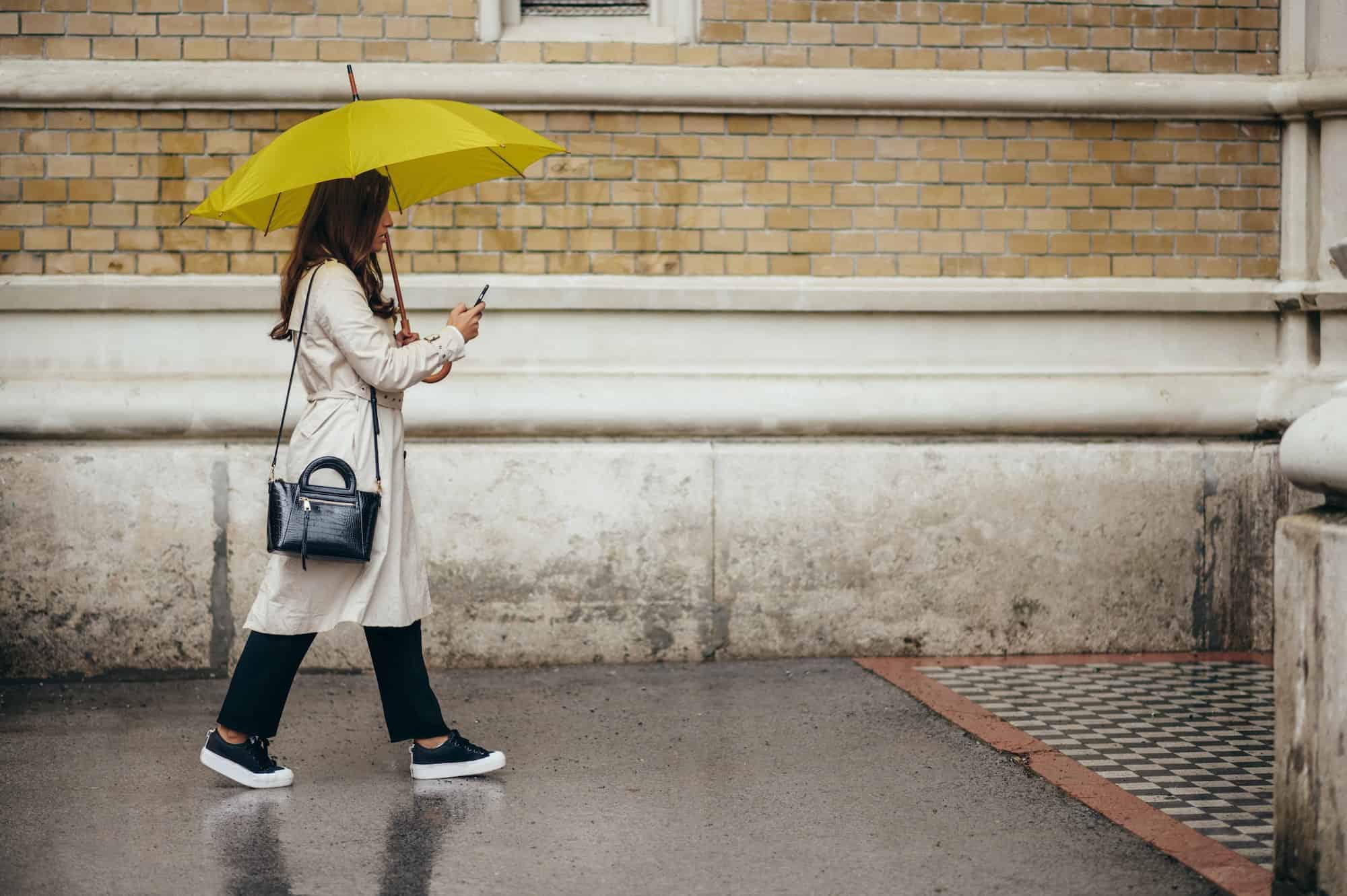 Woman using a smartphone and holding a yellow umbrella while out in the city