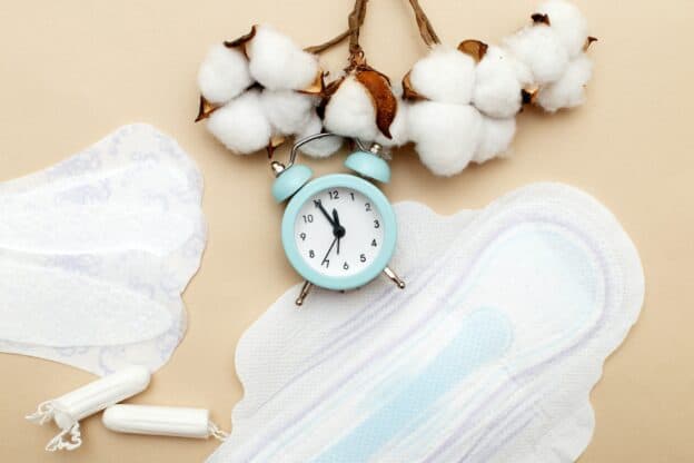 Women's hygiene pads with tampons, flower cotton and alarm clock on beige background