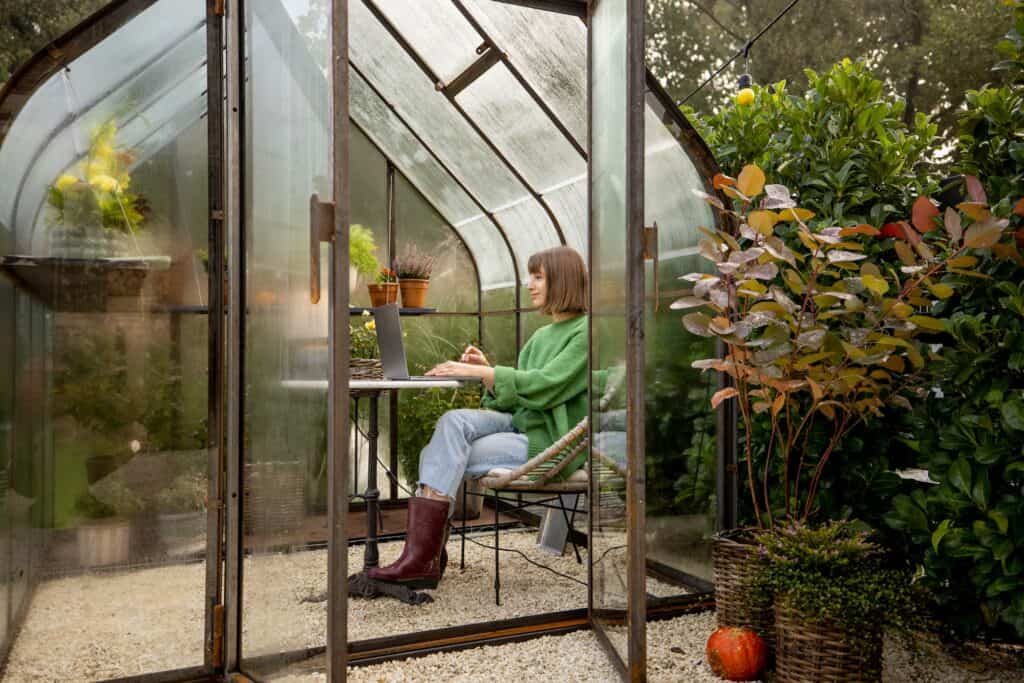 Woman works remotely on laptop in glasshouse at backyard